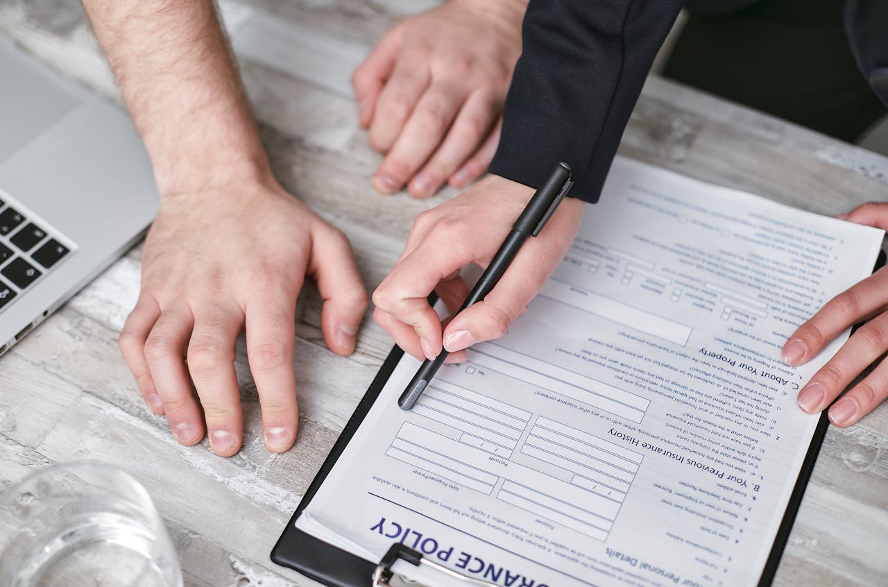 about-02 Close-up image of two people signing an insurance policy document on a wooden desk.