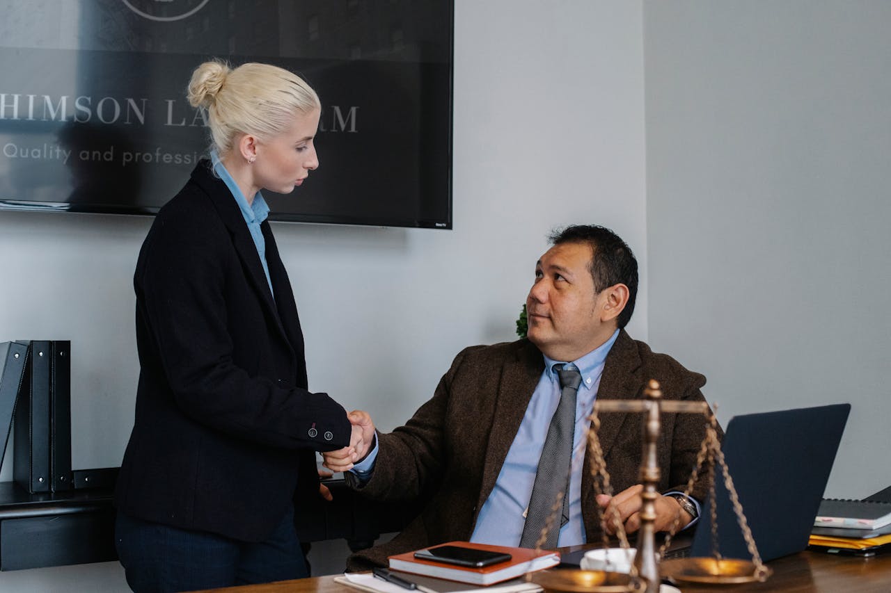 about-05 Multiracial coworkers in formal outfit shaking hands near table with scales of justice