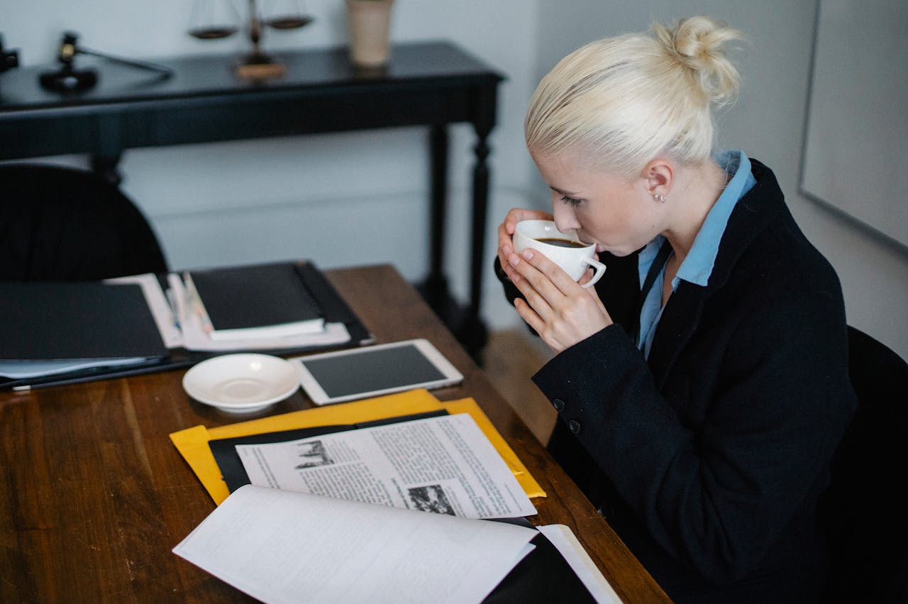 why-choose-us-02 Side view of young concentrated young female judge in formal suit drinking hot coffee while reading case files while sitting at table with stack of documents and tablet