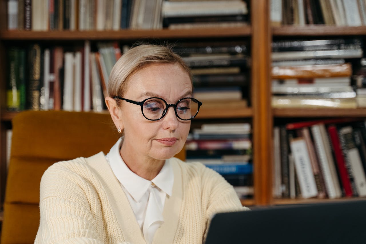 about-07 A senior woman wearing glasses focusing on her laptop in a cozy library environment.